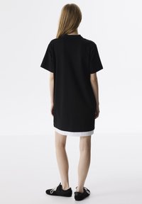 Czarna sukienka o krótkim rękawie i prostym kroju, z białym wykończeniem u dołu, połączona z czarnymi butami. Prosty i minimalistyczny design.