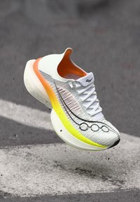 Weißer Sportschuh mit aufwendiger Textur, orangefarbenem Innenraum und gelbem Außensohlen. Verfügt über ein auffälliges schwarzes Logo und Designelement.