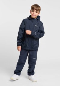 Marineblaue wasserdichte Jacke und Hose, ausgestattet mit elastischen Bündchen, Kapuze und Logos; glatte Textur mit reflektierenden Akzenten.