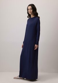 Tumši zils garu piedurkņu maksi kleita, kas izgatavota no mīkstas auduma, ar apaļu kakla izgriezumu un brīvu piegriezumu. Apvienota ar slēgtiem purngaliem austām kurpēm.