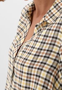 Blusa a quadri con un motivo giallo, marrone e nero, dotata di colletto a camicia e realizzata in un tessuto morbido e strutturato.