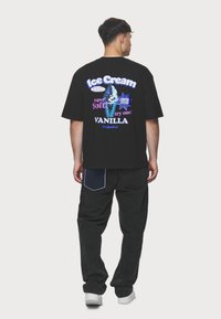 Juodas per didelis t-shirt su spalvingu ledų piešiniu nugaros pusėje. Pora su laisvais juodais džinsais ir baltais sportbatiais.