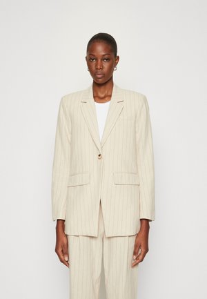 Beige pinstriped blazer dengan satu kancing, kerah notched, dan saku depan, terbuat dari kain bertekstur, dipakai di atas kemeja putih.