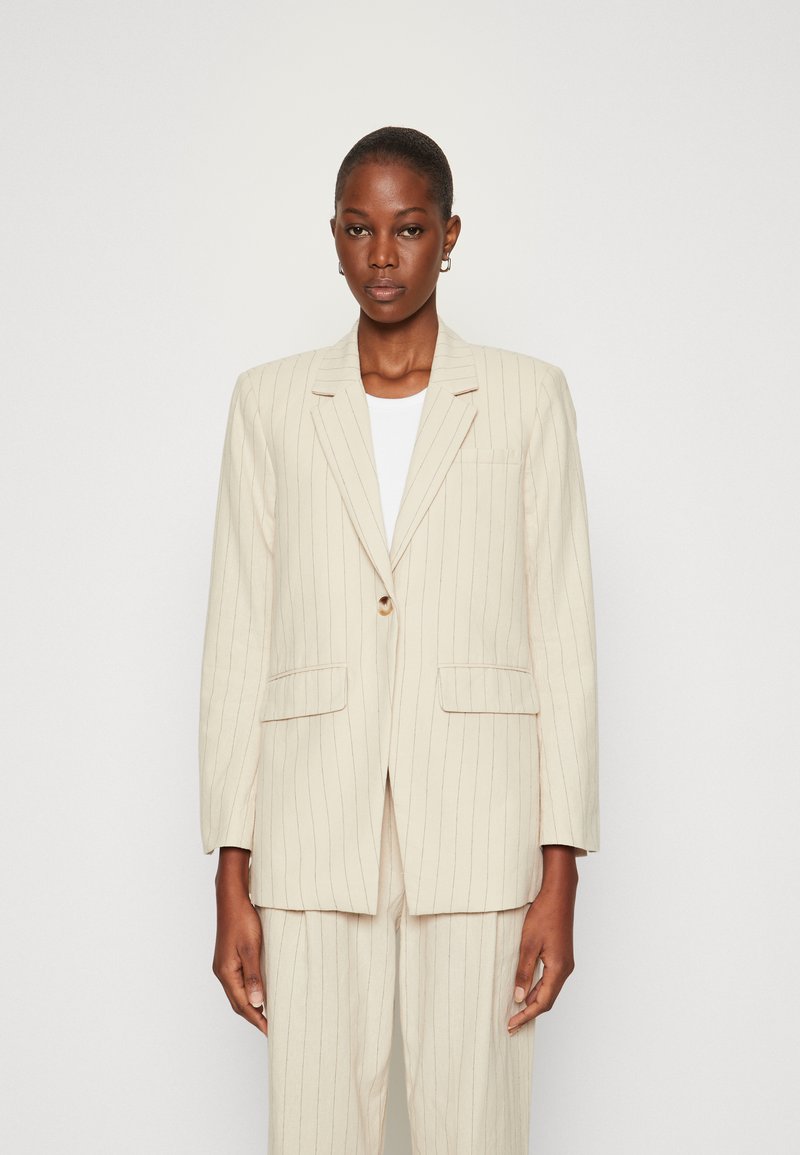 Beige pruhovaný blazer s jedním knoflíkem, klopami a předními kapsami, vyrobený z texturované látky, nošený přes bílou košili.