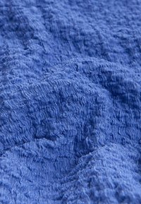 Gros plan sur un tissu bleu texturé avec des motifs ondulés en relief et des plis doux créant une surface tactile.