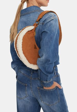 Borsa in suede marrone con bordatura in pelliccia crema, forma curva, tracolla intrecciata e dettagli in oro, indossata sopra una giacca in denim blu.