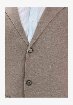 Beigenvärinen napillinen neuletakki vaaleansinisen, valkoisilla raidoilla varustetun kauluksellisen paidan päällä.