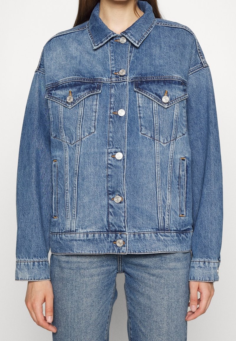 Chaqueta de denim en azul claro con un diseño clásico, que presenta dos bolsillos en el pecho, botones plateados y un corte ligeramente oversize.