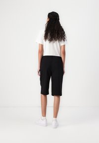 Shorts bermuda noirs en tissu léger, arrivant aux genoux, présentant un design simple avec une texture lisse, associés à un t-shirt blanc.