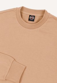 Chemise marron clair à manches longues avec poignets et col côtelés, avec une étiquette Colmar Originals noire et rouge au niveau de l'encolure.