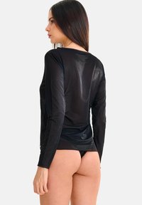 Haut noir transparent à manches longues avec une texture douce, doté d'un col rond, d'une coupe ajustée et d'un léger éclat.