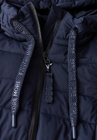 Námořnická puffer bunda se zapínáním na zip, s pletenými šňůrkami s textem "Explore More" a gumovým logem.