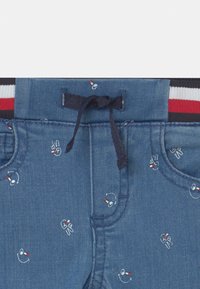 Szorty dżinsowe z niebieskiego materiału z zabawnymi wzorami, w tym haftowanymi uśmiechniętymi buźkami, w zestawieniu z paskiem elastycznym w paski.