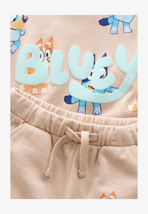 Svetlo bež majica s kapuco z igrivimi ilustracijami psov in besedo "BLUEY" v nežno akvamarinskih črkah; kombinirana z ujemajočimi svetlo bež trenirkami z vrvico v pasu.