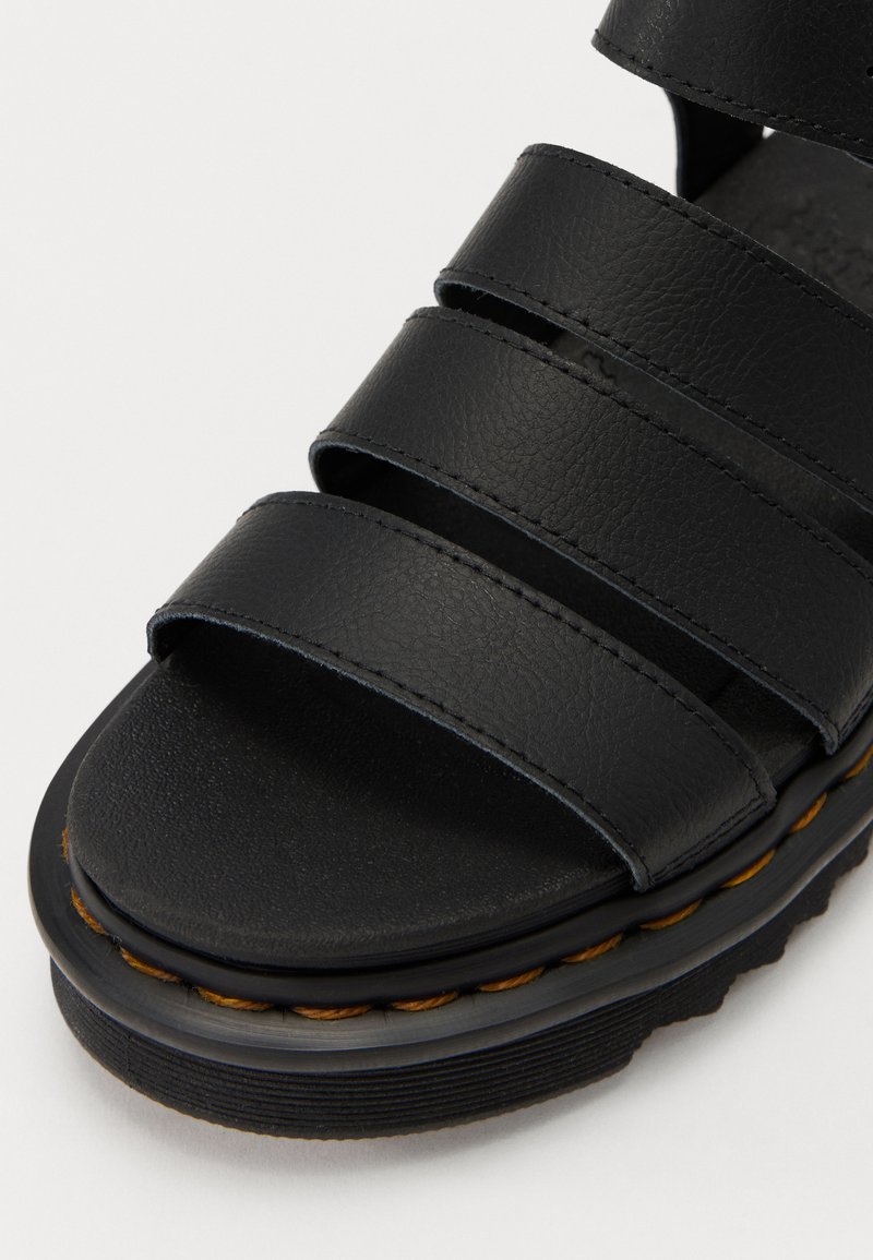 Sandal nera realizzata in materiale sintetico testurizzato con tre larga cinghie, punta arrotondata e suola spessa con un dettaglio di cucitura gialla.