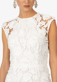 Abito bianco in pizzo floreale con finitura testurizzata, maniche a cappuccio e silhouette aderente, caratterizzato da intricati motivi floreali in tutto il tessuto.