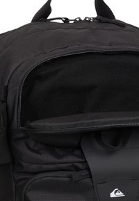 Czarny plecak z teksturowanej tkaniny, z zamkiem błyskawicznym i wewnętrzną kieszenią. Gładkie akcenty i logo na klapie.