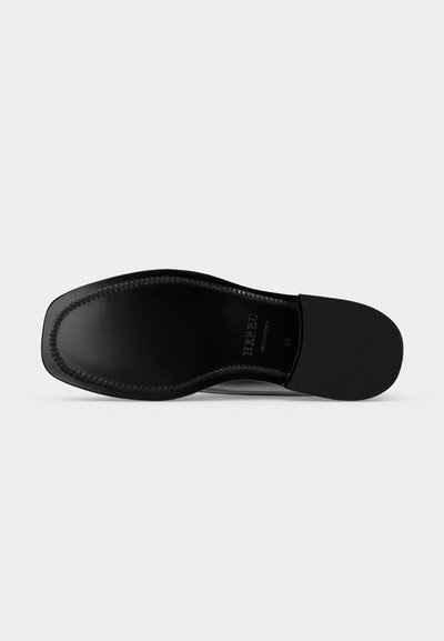 Semelle de chaussure en cuir noir avec couture visible autour du bord et indication de la taille près du talon sur un fond clair uni.