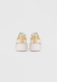 White and gold platform sneakers with a smooth leather finish and rounded back. Features embossed logo and textured sole for grip.
