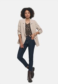 Beige Blazer über einem schwarz-braun gemusterten Oberteil, kombiniert mit dunklen Skinny Jeans und braunen Ankle Boots mit dicken Sohlen.