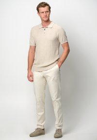 Beige kortärmad polo-shirt med en strukturerad mönster, treknappslå, matchad med vita smala byxor och ljusbeige sneakers.