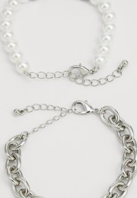 Deux bracelets : l'un avec des perles blanches et un fermoir en argent, l'autre une chaîne en argent épaisse avec un fermoir en forme de homard et une chaîne d'extension.