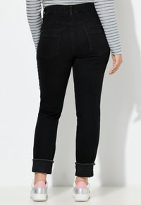 Jeans de denim negros con una cintura alta, corte ajustado y dobladillos deshilachados. Los bolsillos traseros son visibles, combinados con zapatillas plateadas y rosas.