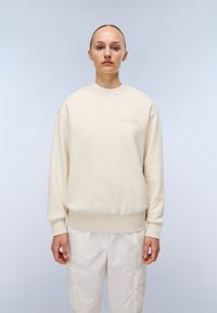Beige sweatshirt met ronde hals en geribbelde manchetten en zoom, met een getextureerd logo op de borst, gecombineerd met witte cargobroek.