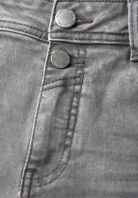 Tissu en denim gris avec deux boutons en métal à la taille, des coutures marquées et une texture subtile ; présente un design classique de poche de jean.