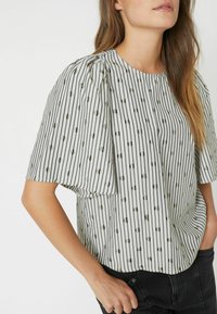 Blusa a righe con maniche a sbuffo, caratterizzata da strisce sottili nere e crema alternate, motivo a pois e scollatura rotonda.