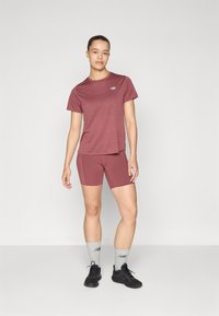 T-shirt de sport bordeaux et shorts assortis en tissu respirant. Des baskets noires et des chaussettes grises avec logo complètent la tenue.