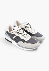 Pár šedých a bílých sportovních tenisek se symbolem lebky a zkřížených kostí na boku a bílými šňůrkami, nakloněných tak, aby ukázaly boční a vrchní pohled.