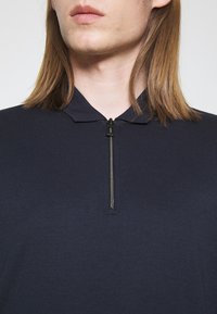 Polo bleu marine côtelé avec une fermeture éclair courte et un col classique, confectionné dans un tissu doux et texturé.