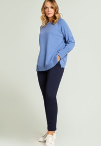 Suéter de algodón azul claro con cuello redondo y ribete acanalado, combinado con pantalones ajustados azul marino y zapatillas blancas.