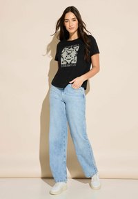 Černé tričko s grafickým potiskem, světle modré oversize džíny a bílé tenisky. Hladký materiál a volný střih s krátkými rukávy.