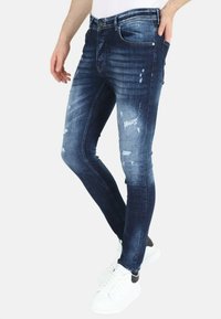 Donkerblauwe versleten skinny jeans met een vervaagde wassing, voorzien van scheuren en subtiele wassing, gedragen met witte sneakers.