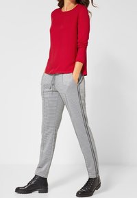 Camicia rossa a maniche lunghe abbinata a pantaloni grigi a quadri con cordino e righe laterali, completata da stivaletti neri con lacci.