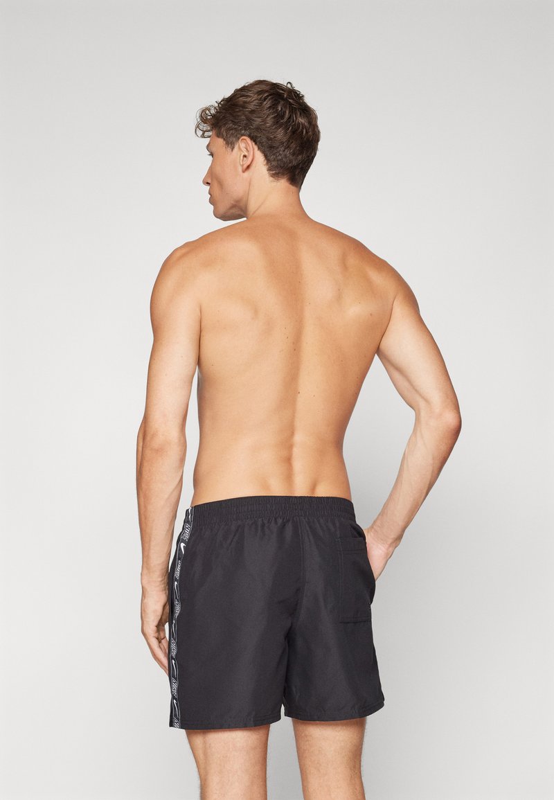 Pantaloni da bagno neri con vita elastica e tasche laterali, caratterizzati da una striscia a logo a contrasto lungo i lati. Texture liscia, lunghezza a metà coscia.