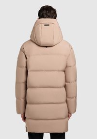 Abrigo de invierno beige acolchado con un cuello alto y una gran capucha. El material es suave, con secciones acolchadas horizontales y un corte ajustado.