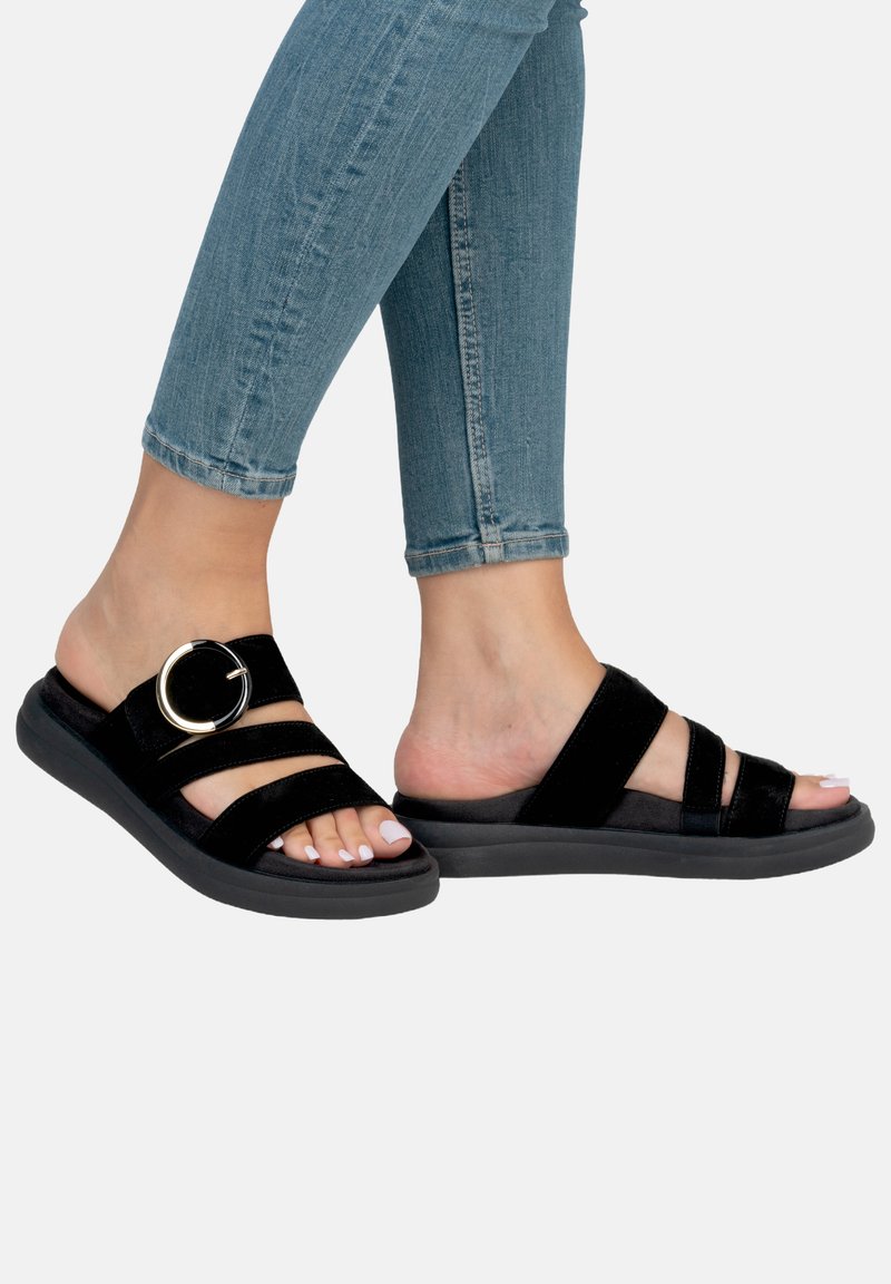 Black suede sandals with three wide straps, featuring a circular gold hardware accent, set on a sturdy black sole.