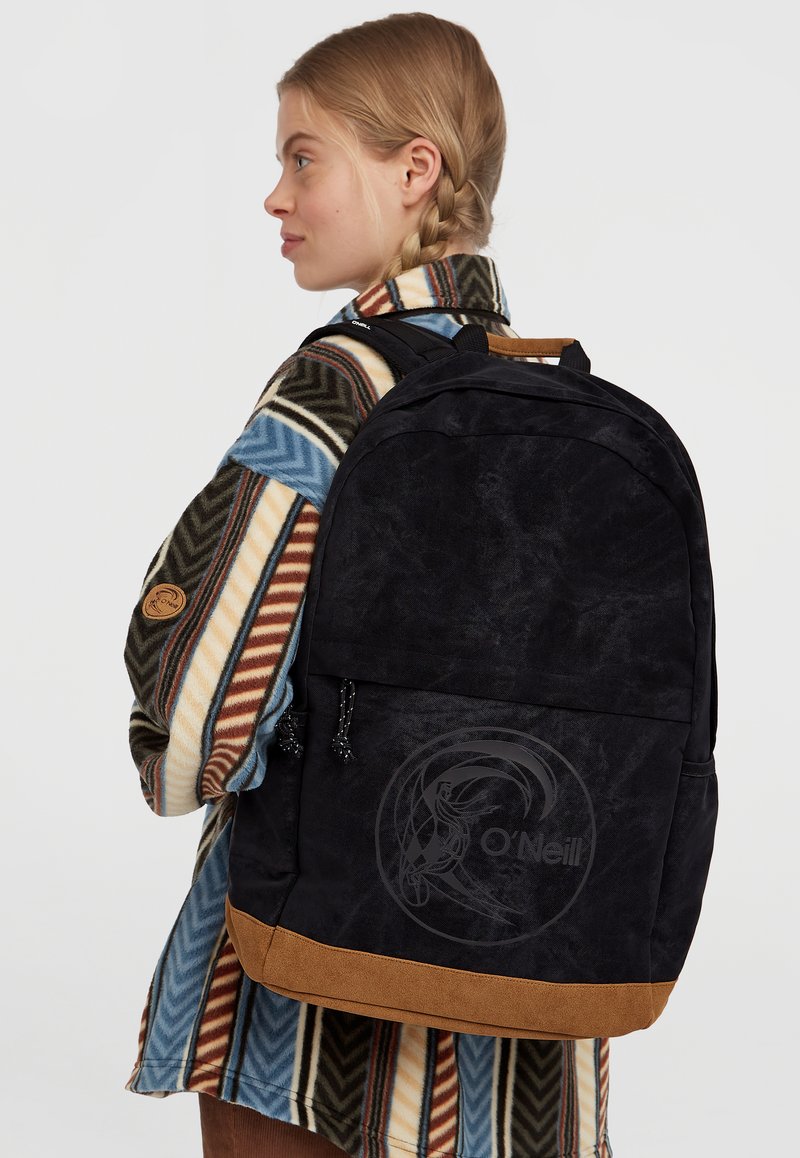 Zwarte rugzak met een zachte textuur, voorzien van een tan suede onderkant, een logo aan de voorkant en verstelbare schouderbanden. Gestyled met een gestreepte buitenlaag.
