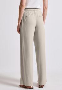 Pantalons larges beige clair avec une taille élastique, dotés de deux poches arrière et d'une texture de tissu lisse. Coupe longue au sol.
