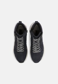 Marinblåa träningsskor har en texturerad yta, silverfärgade skosnören, sidodragkedja och en vit gummisula. Inredningen som visas är vadderad för komfort.