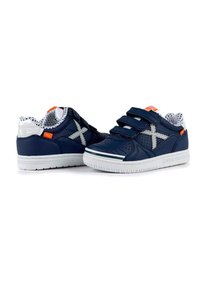 Zapatillas de deporte azul marino con suelas blancas, presentan una parte superior de malla, tiras de Velcro, detalles en plata y un toque naranja en la lengüeta.
