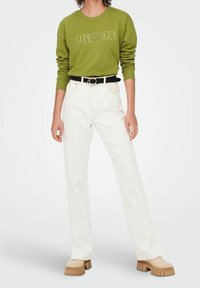 Zelená mikina s nápisem "COPENHAGEN", doplněná bílými kalhotami s rovnými nohavicemi a černým opaskem. Obuv je hnědá na platformě s strukturovanou podrážkou.