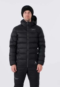 Czarna pikowana kurtka puchowa z poziomym wzorem przeszyć, zamkiem z przodu i kapturem. W komplecie pasujące pikowane spodnie puchowe oraz czarna czapka beanie.