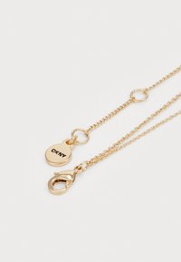 Collana a doppio strato in oro con un ciondolo circolare etichettato "DKNY" e un gancio a molla, caratterizzata da un delicato texture a link.