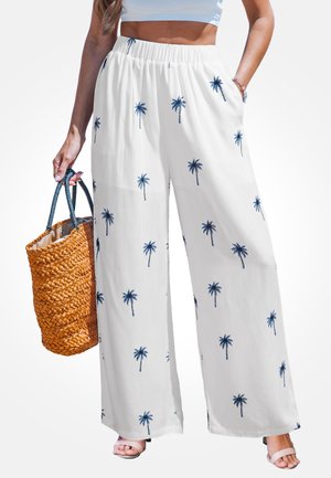 Weiße Hose mit weitem Bein mit blauen Palmen-Prints, getragen mit weißem Crop Top, dazu eine geflochtene Strohtasche und beige Sandalen.