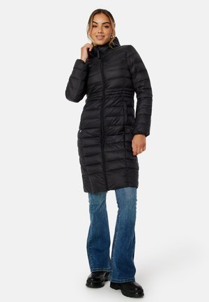 Zwarte pufferjas met een hoge kraag, verticale stiksels en ritssluiting. Draag het over lichtblauwe flared jeans en zwarte laarzen.