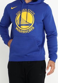 Sudadera azul hecha de una tela suave que presenta un gran logo amarillo de "Golden State Warriors" y una capucha con cordones, con un bolsillo canguro.
